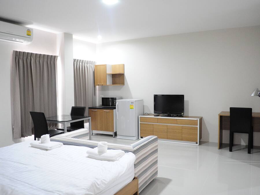 A modern hotel room with a bed, a desk, a television, and a kitchenette.