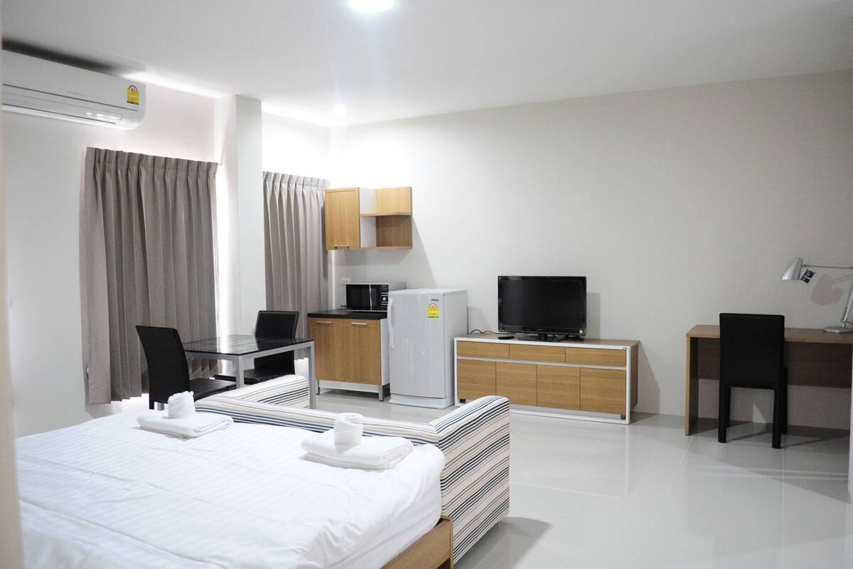 A hotel room with a bed, a desk with a computer, a television, a refrigerator, and a microwave.