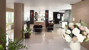 Een moderne hotellobby met een receptiebalie, een zithoek en een grote bloemenvaas.