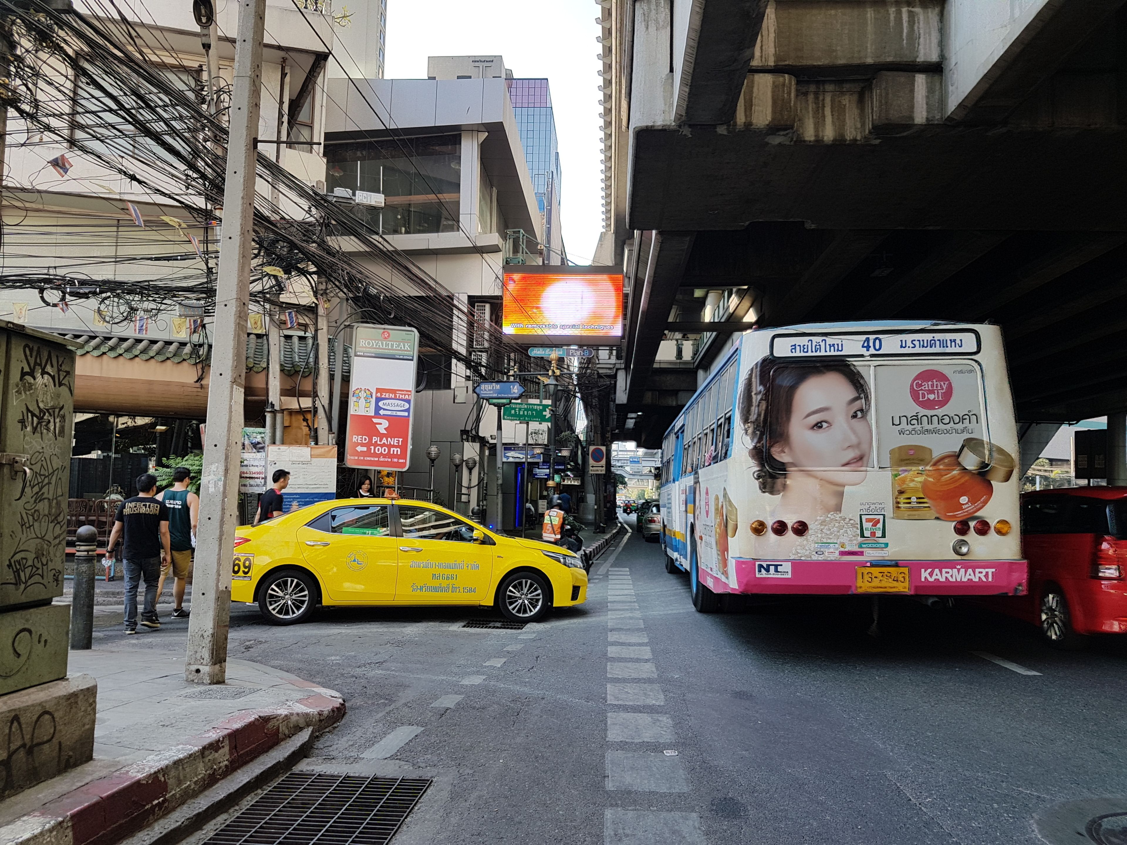 Una calle urbana concurrida con un taxi amarillo y un autobús de dos pisos.