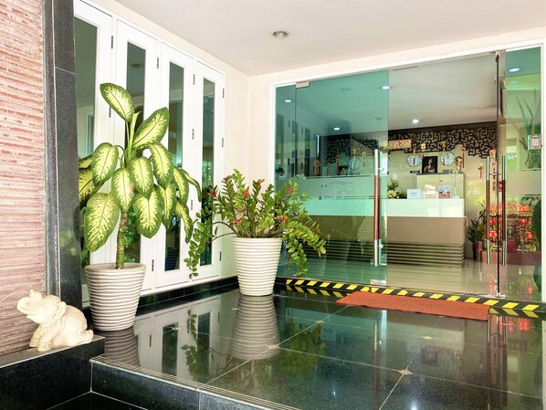 Un área de recepción con diseño moderno, que incluye un mostrador de recepción, plantas en macetas y una estatua decorativa de elefante.
