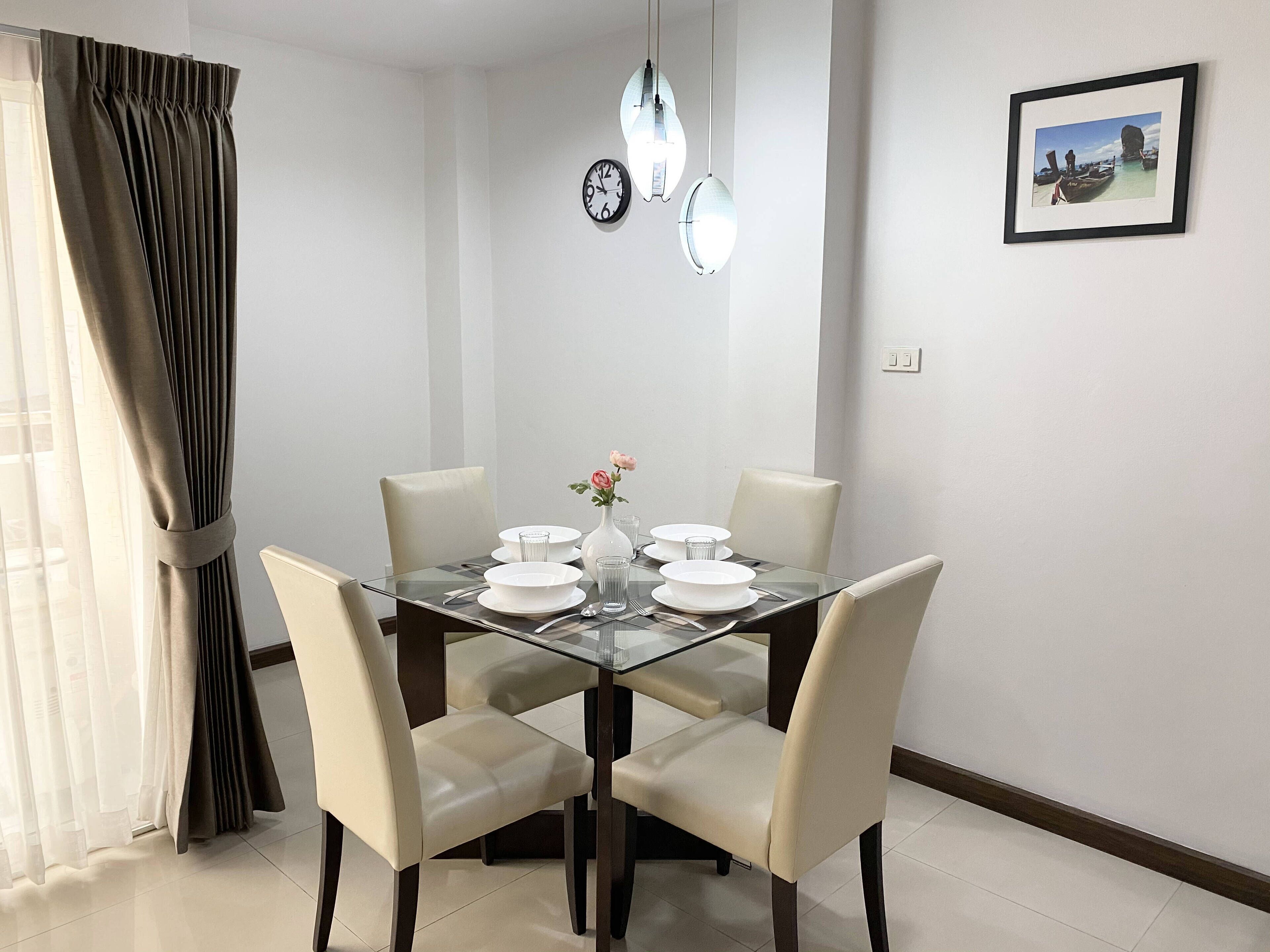 A dining area with a glass table, white chairs, and a vase with flowers.