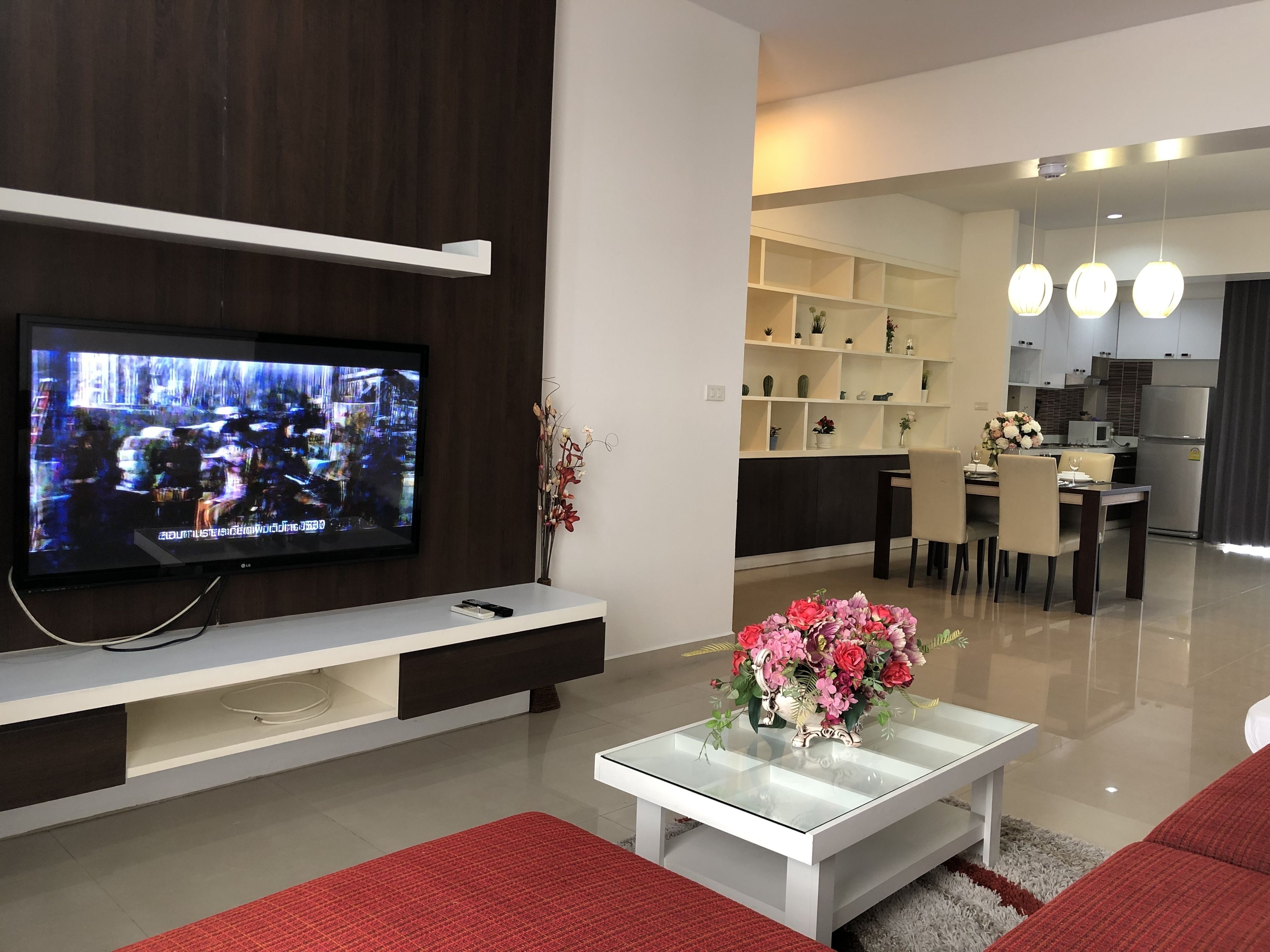 A modern living room with a flat-screen TV, a glass coffee table with a floral centerpiece, and a red rug.