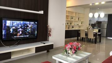 A modern living room with a flat-screen TV, a glass coffee table with a floral centerpiece, and a red rug.