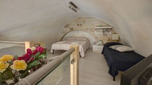A bedroom with a stone arch ceiling, two beds, a bedside table, a nightstand, and a small shelf. - B&B Frugis (Polignano a Mare)