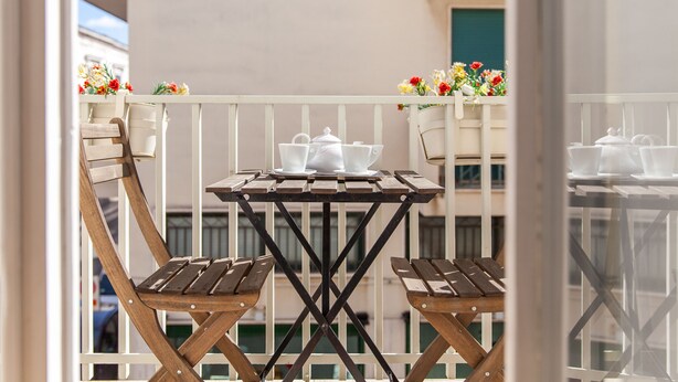 A balcony with a small table and two chairs, a white railing, and flower boxes with flowers. - B&B Frugis (Polignano a Mare)