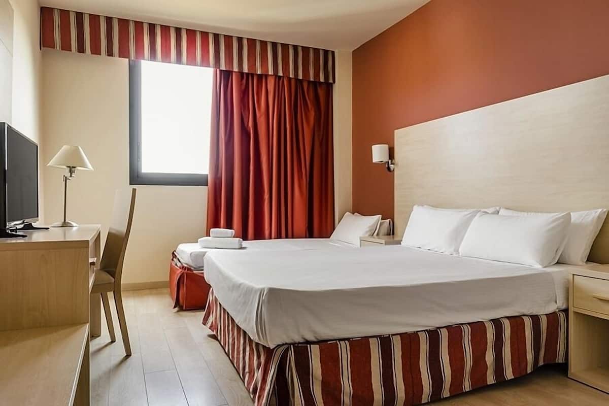 Une chambre d’hôtel équipée d’un lit, d’un bureau, d’une chaise, d’une télévision, d’une lampe et d’une fenêtre avec des rideaux.