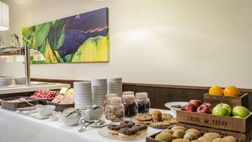 Una mesa de buffet con diversos alimentos, como frutas, galletas y pasteles, y un cuadro en la pared.