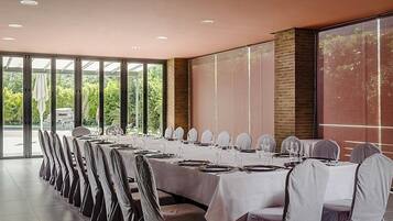 A long dining table set for a formal event, with chairs covered in white fabric, in a room with large windows and a brick wall.