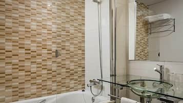 Un bany modern amb banyera amb envà de vidre, un lavabo de vidre i una dutxera amb envà de vidre.