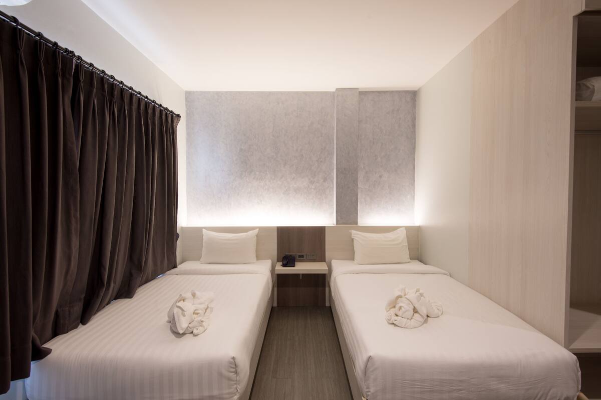 A hotel room with two beds, a nightstand, and a large window with curtains.