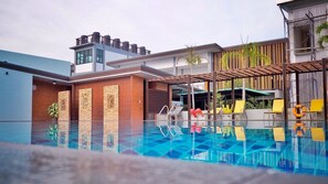 A modern hotel with a swimming pool, outdoor seating, and a mix of contemporary and traditional architecture.