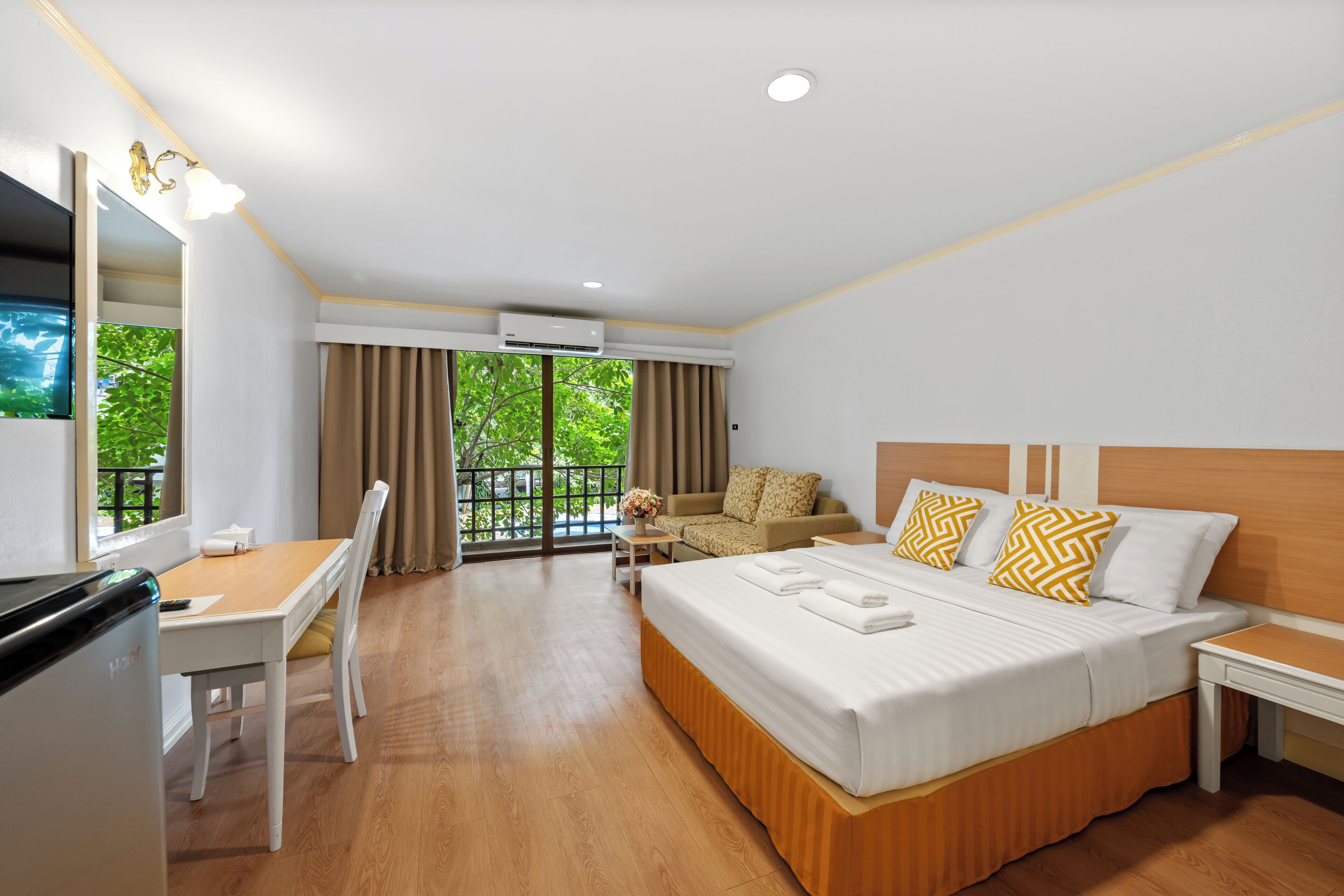 Ein Hotelzimmer mit Bett, Schreibtisch, Stuhl, einer Couch und einem Balkon mit Blick ins Grüne.