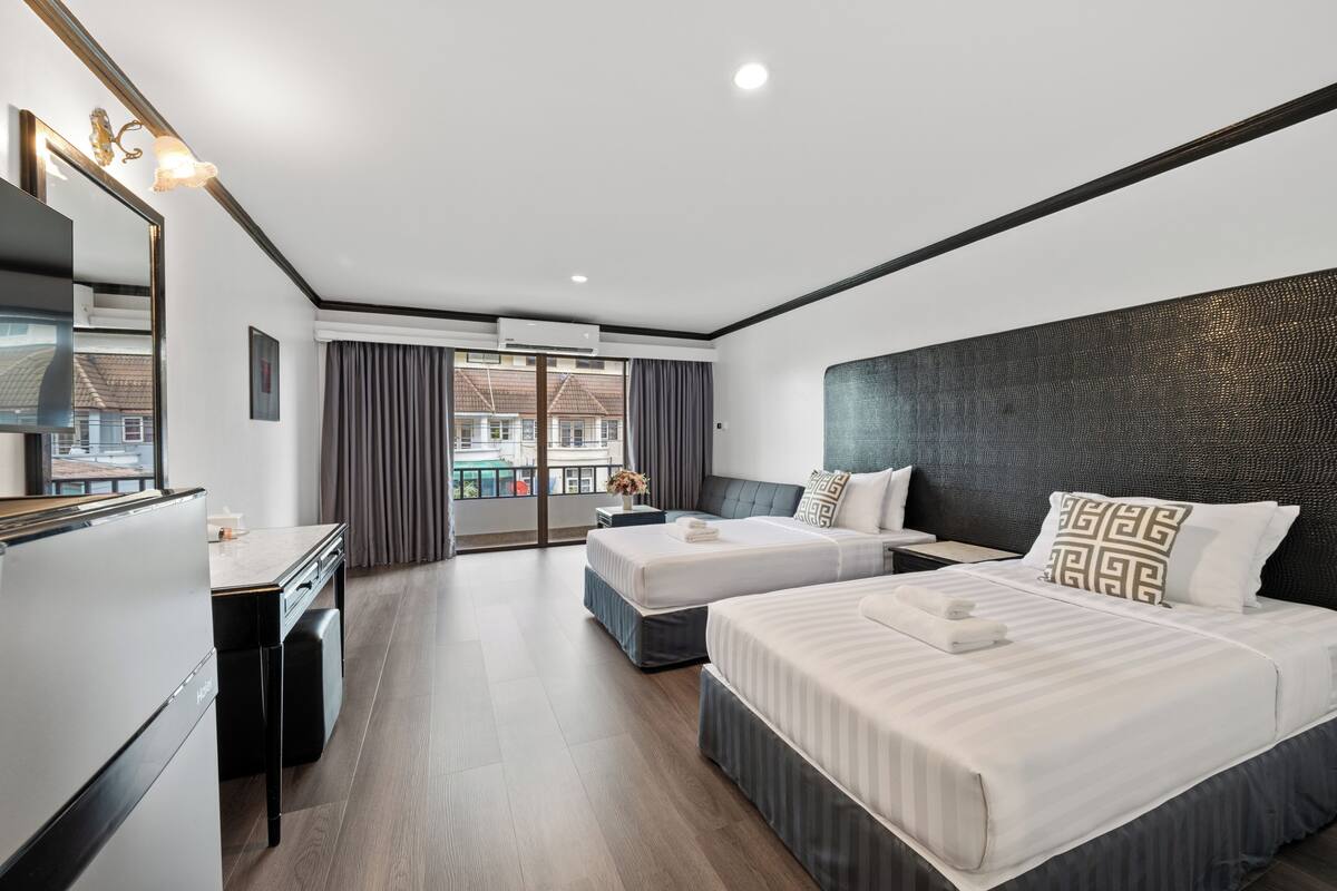 A hotel room with two beds, a desk, and a large window with curtains.