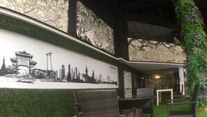 Un restaurant décoré d’une fresque représentant le paysage urbain de Bangkok, doté de meubles en osier et d’un mur végétal orné de plantes grimpantes.