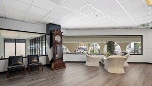 Une salle d’attente dotée de fauteuils en cuir, d’une grande horloge murale, de fauteuils en osier et offrant une vue sur la rue grâce à de grandes fenêtres.