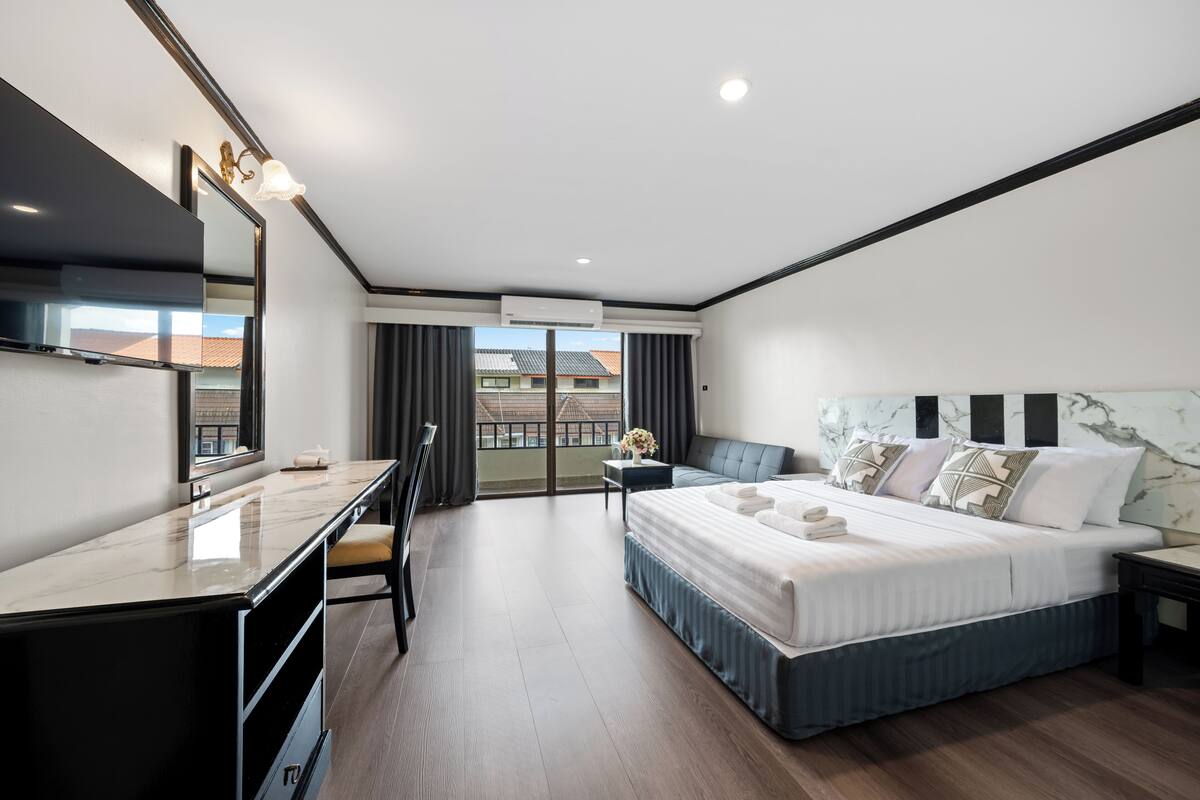 A modern hotel room with a large bed, a desk, and a balcony with a view.