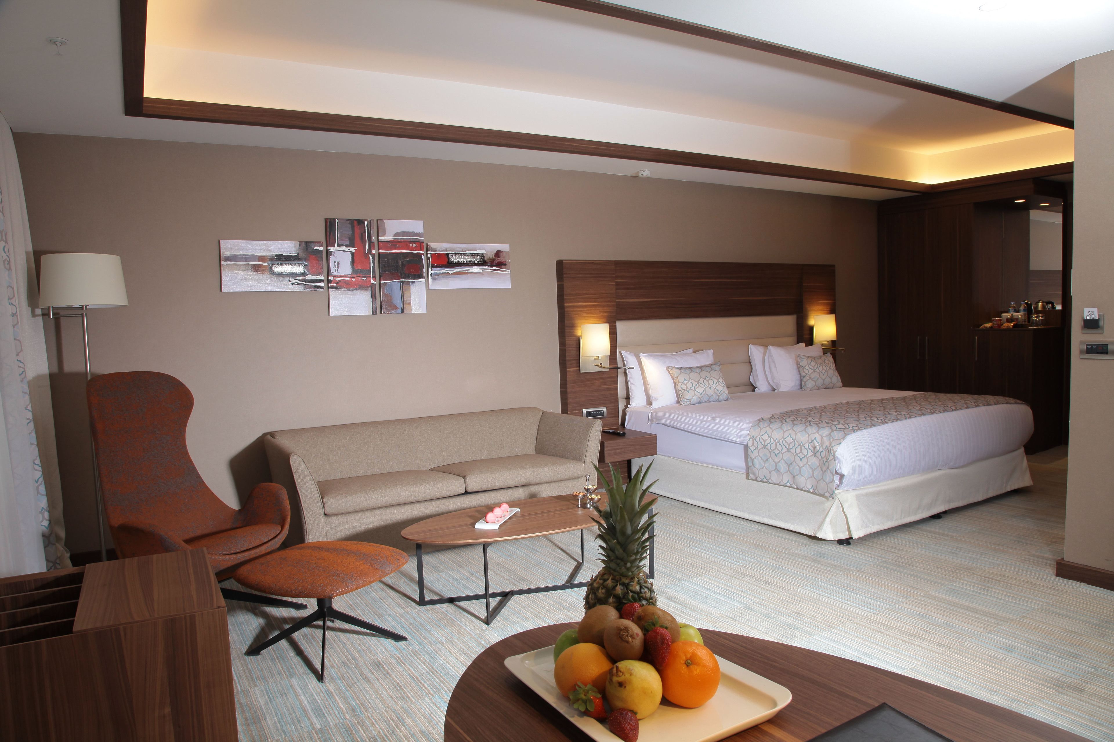 A hotel room with a bed, a sofa, a coffee table, and a fruit bowl.