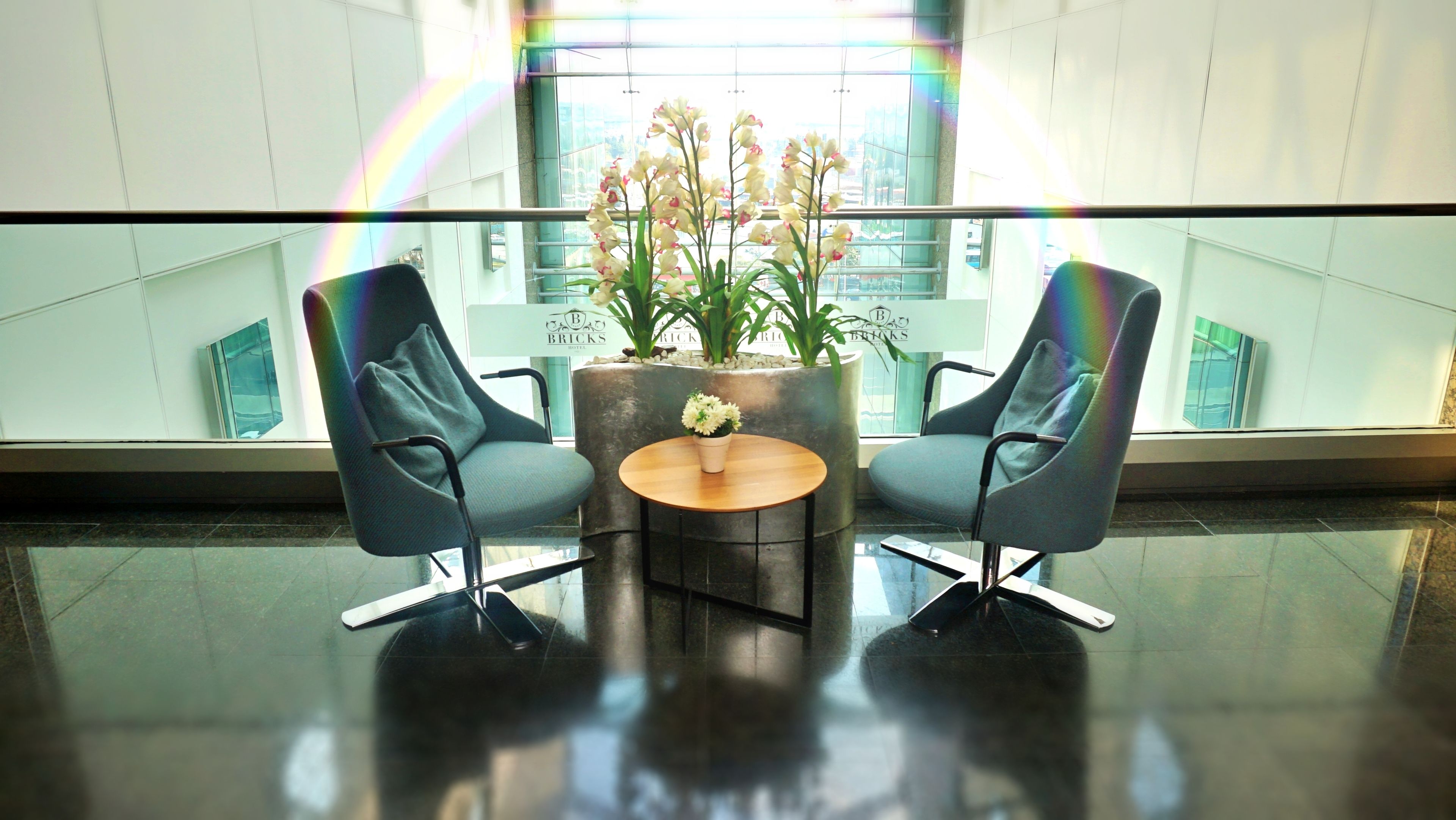 Eine moderne Lobby mit zwei schwarzen Sesseln, einem runden Holztisch und einem Blumentopf mit Blumen.