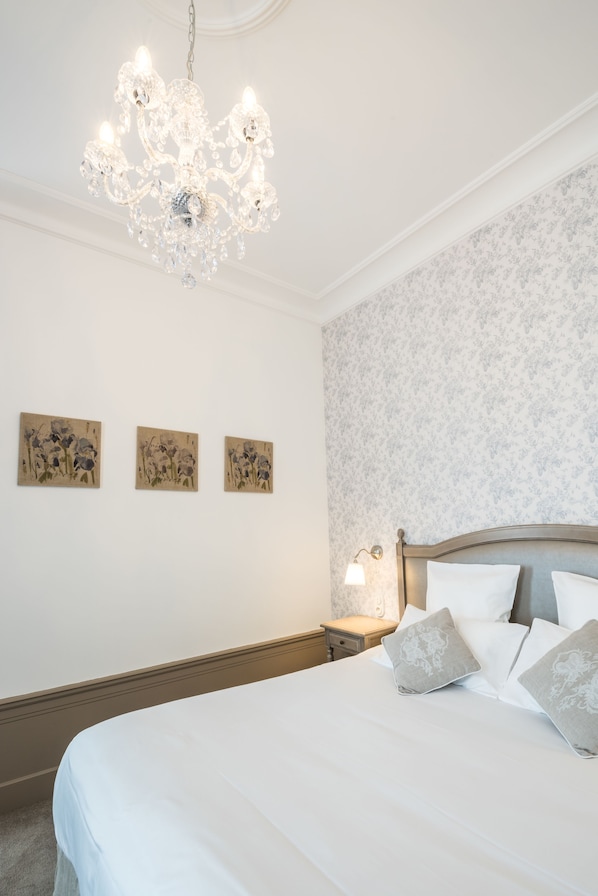 A bedroom with a large bed, a chandelier, and three wall-mounted paintings.