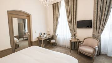 A hotel room with a large bed, a desk, a chair, a television, and a chandelier.