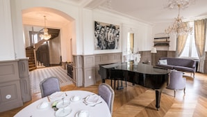 Un comedor con piano, una araña y una escalera que lleva a otra habitación.
