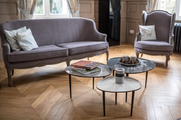 A living room with a grey sofa, two armchairs, and two small round tables with books and decorative items. - Château de Montabert (Montaulin)