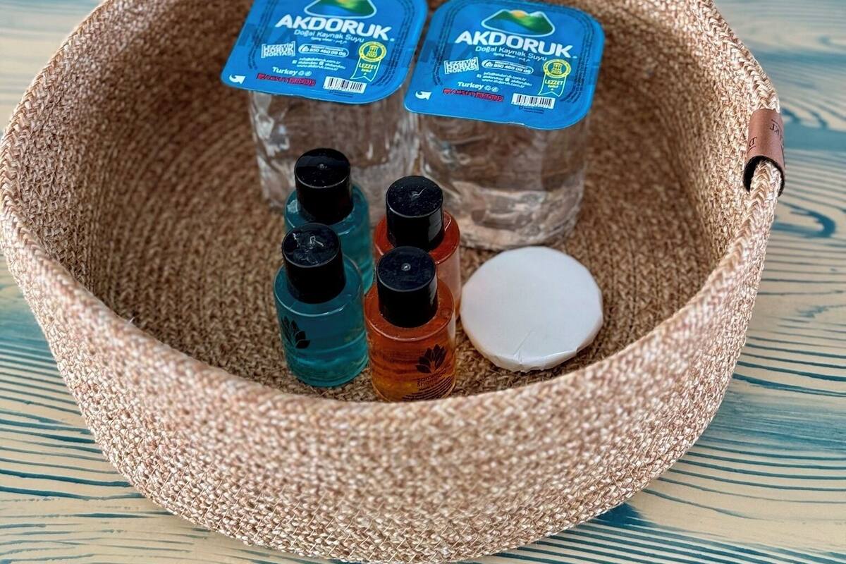 A woven basket containing two blue-lidded containers labeled "AKDORUK," a white lid, and three small bottles in teal, orange, and black.