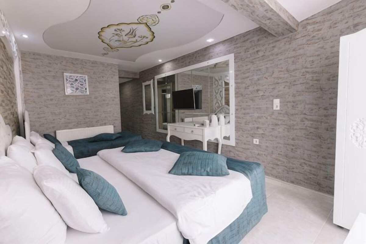 A bedroom with two beds, a white dresser, a large mirror, and a ceiling with a decorative design.