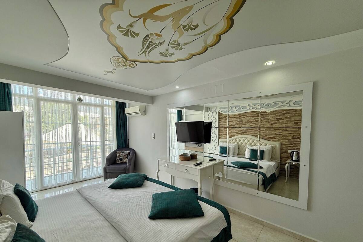 A modern bedroom with a large bed, a desk, a TV, and a mirrored wardrobe.