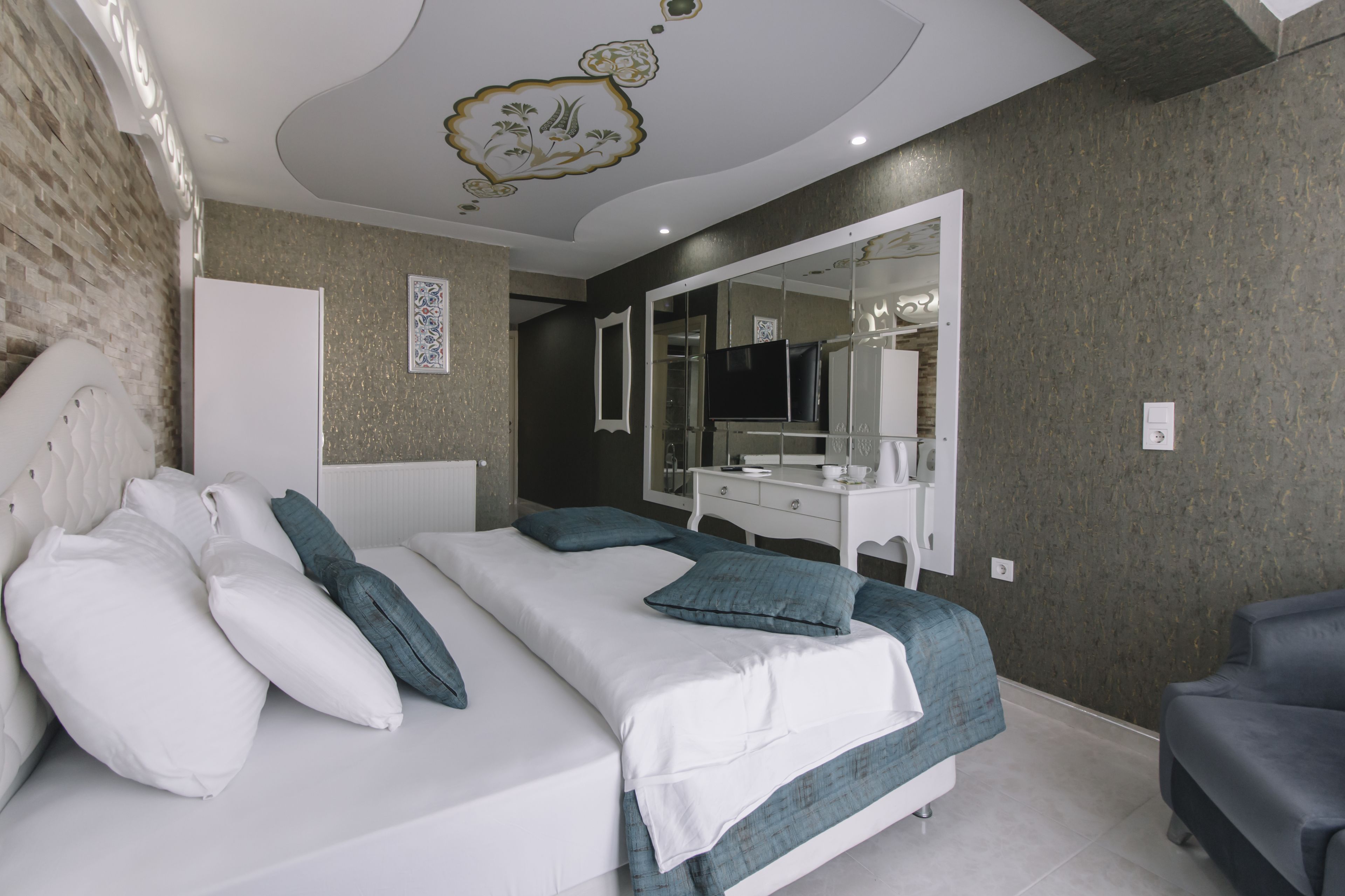 A modern bedroom with a large bed, a vanity with a mirror, and a television.