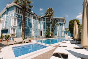 A pool area with lounge chairs and a large building with blue siding and white trim.