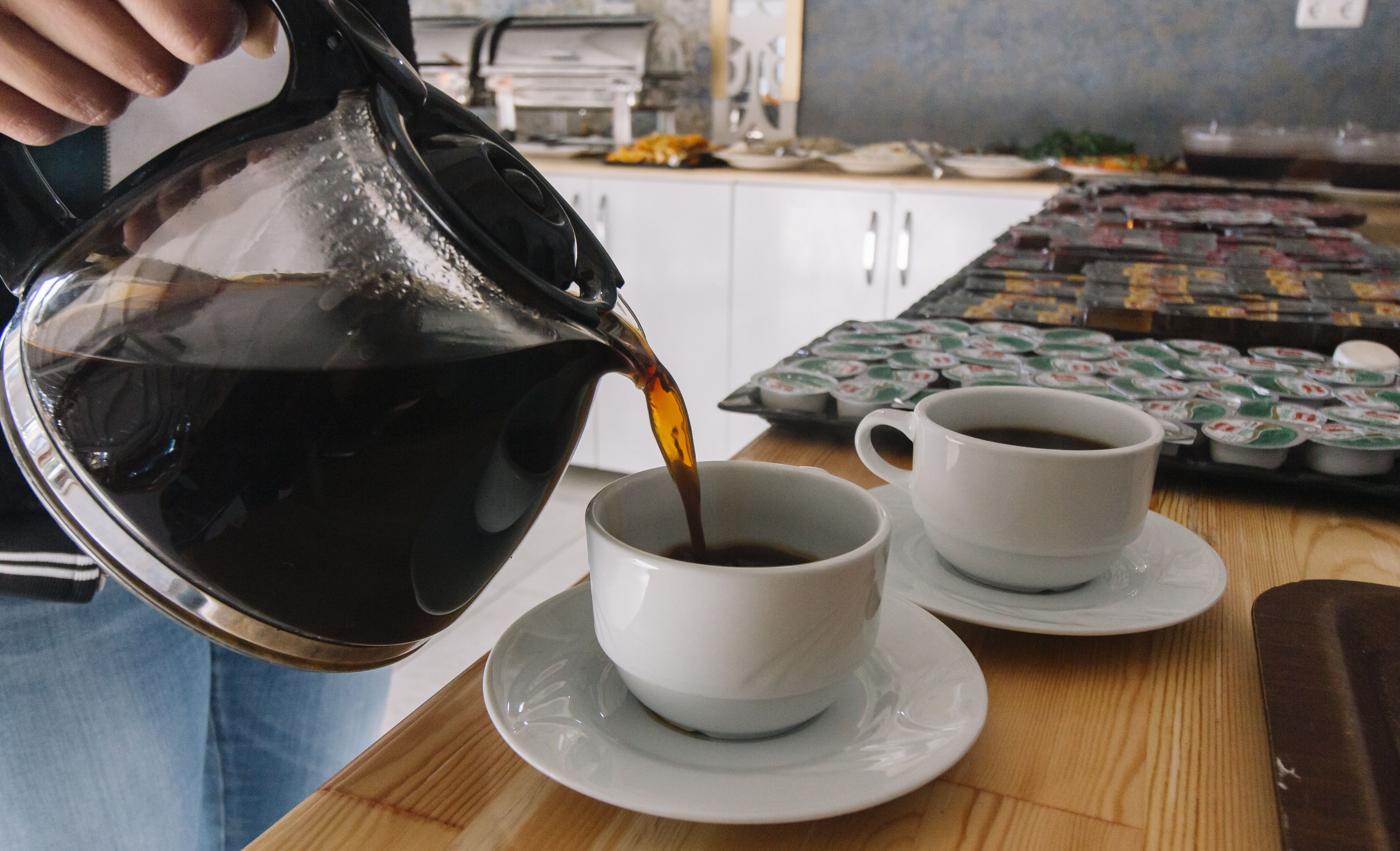 Uma pessoa a servir café numa chávena, com outra chávena e pires por perto.