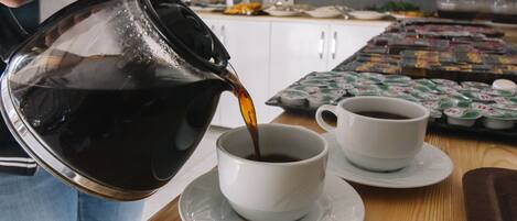 Una persona sirviendo café en una taza sobre una mesa, con otra taza y platillo cerca.