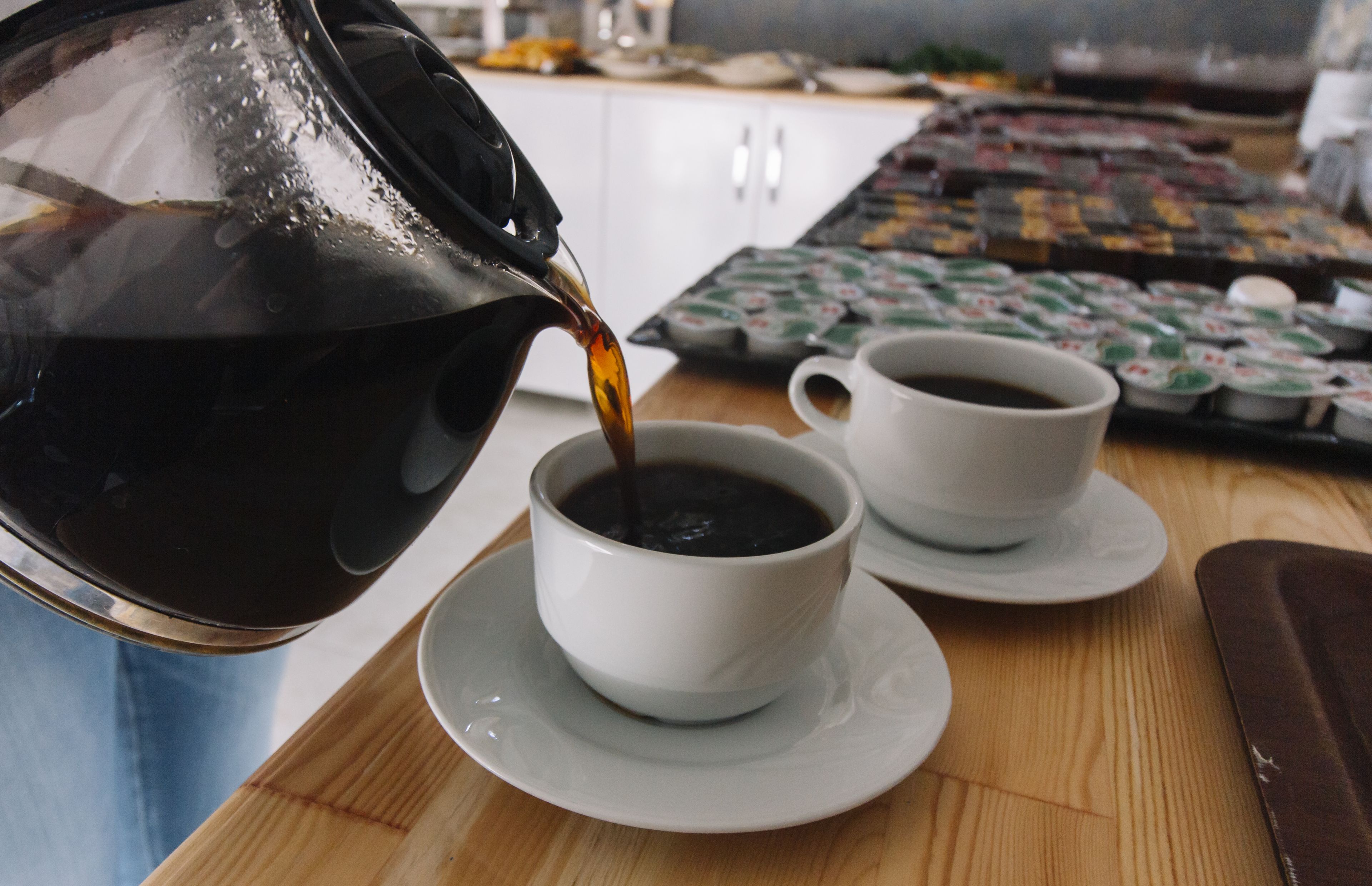 Una cafetera sirve café en una taza sobre una mesa de madera.
