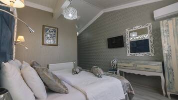 Una cama bien hecha con almohadas, una lámpara de noche, un espejo decorativo y un aparador con un televisor encima.
