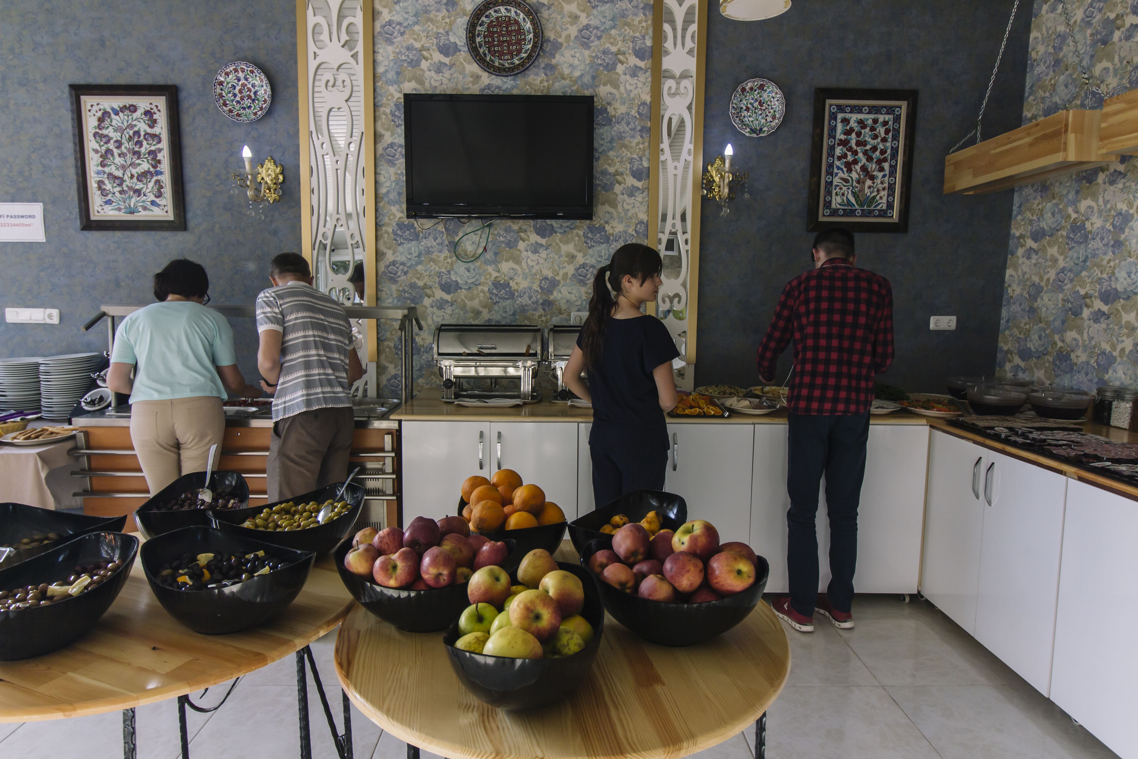 A kitchen area with a buffet setup, including bowls of fruits and vegetables, and a television mounted on the wall.