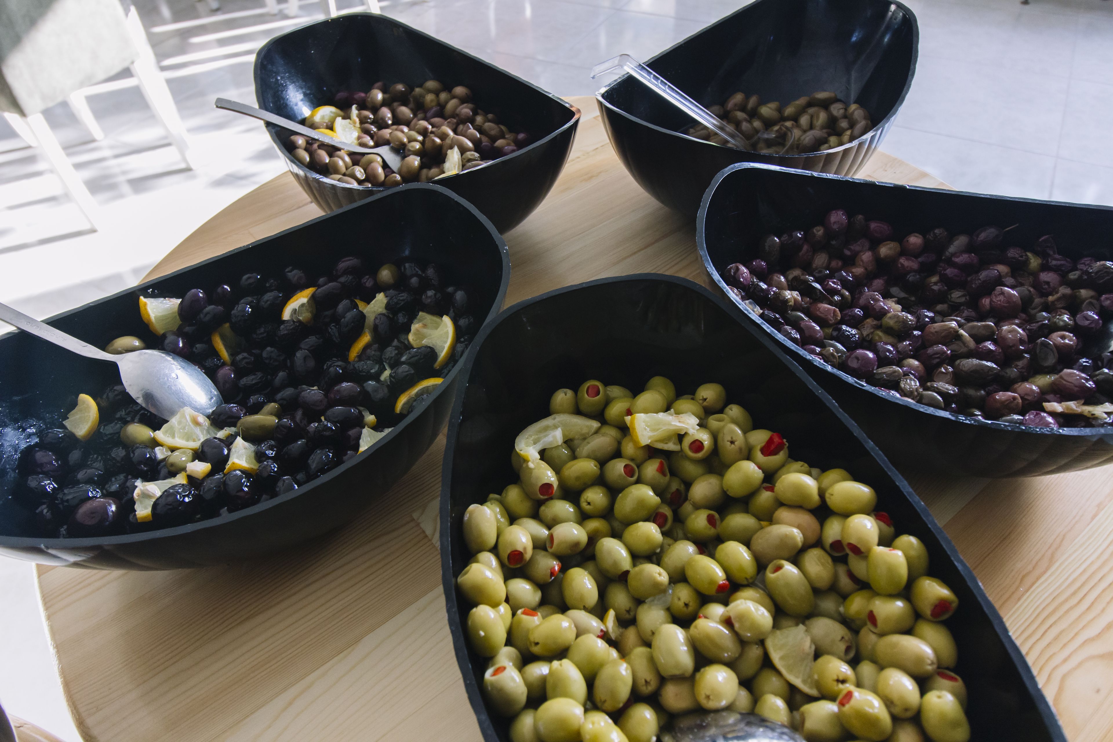 A wooden table with five black bowls containing olives, lemons, and other ingredients.