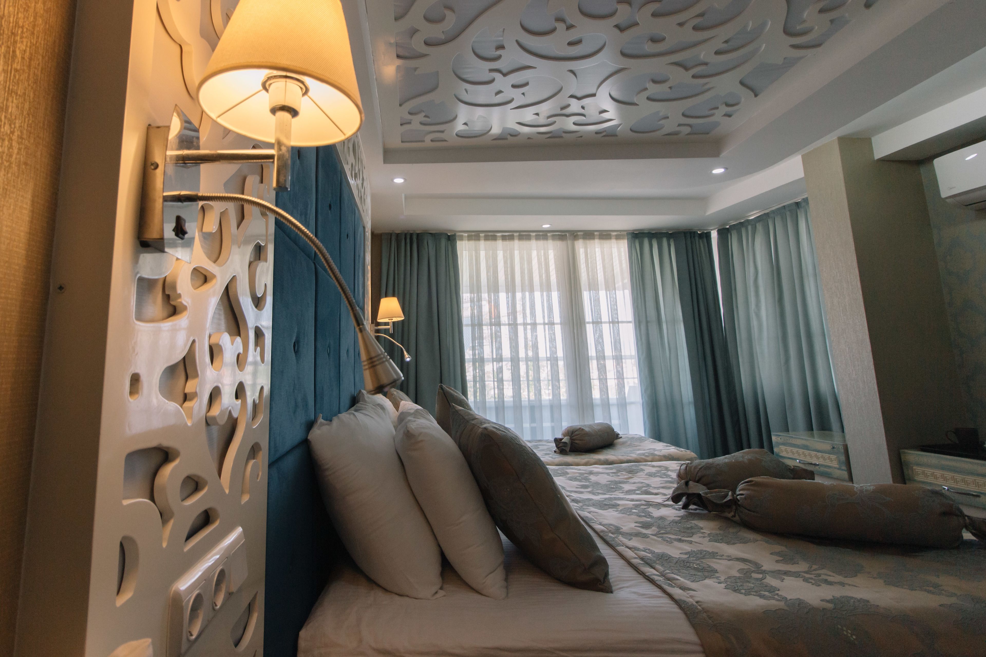 A hotel room with a bed, two lamps, a decorative ceiling, and a window with curtains.