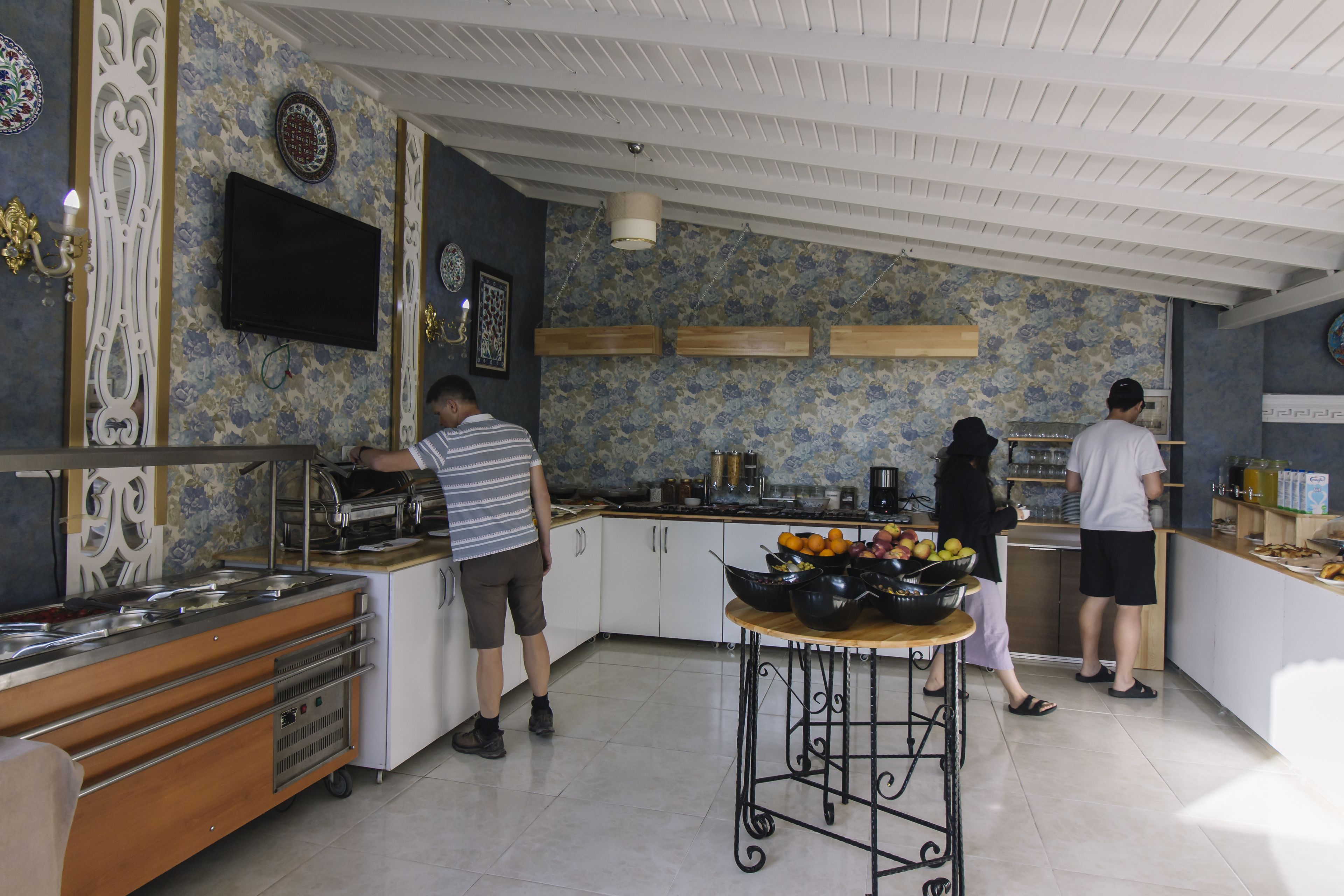 Cozinha com serviço de buffet, televisão na parede e painel decorativo com motivos florais.