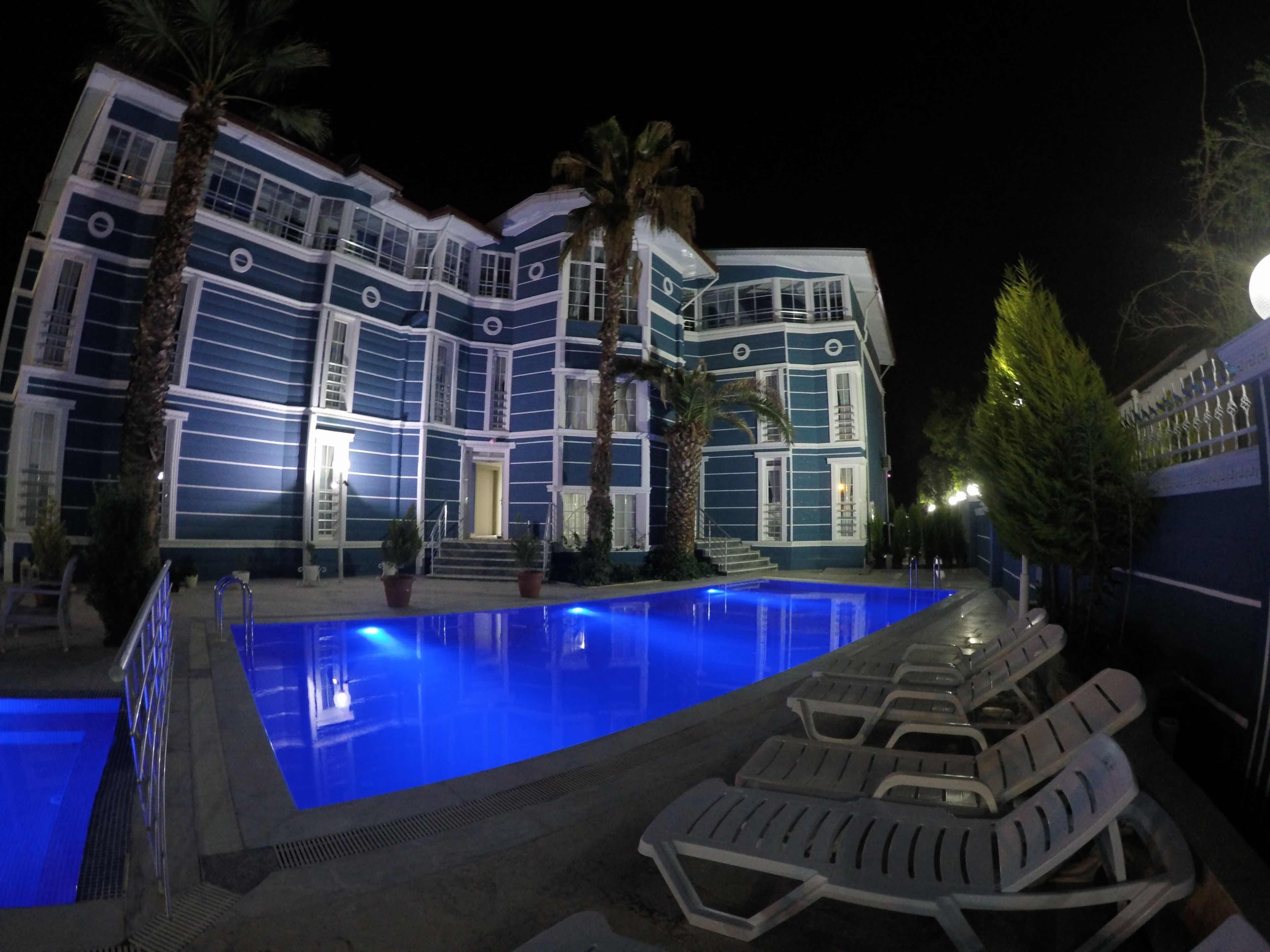 Un área de piscina con sillones de descanso y un edificio con paredes exteriores azules y blancas.