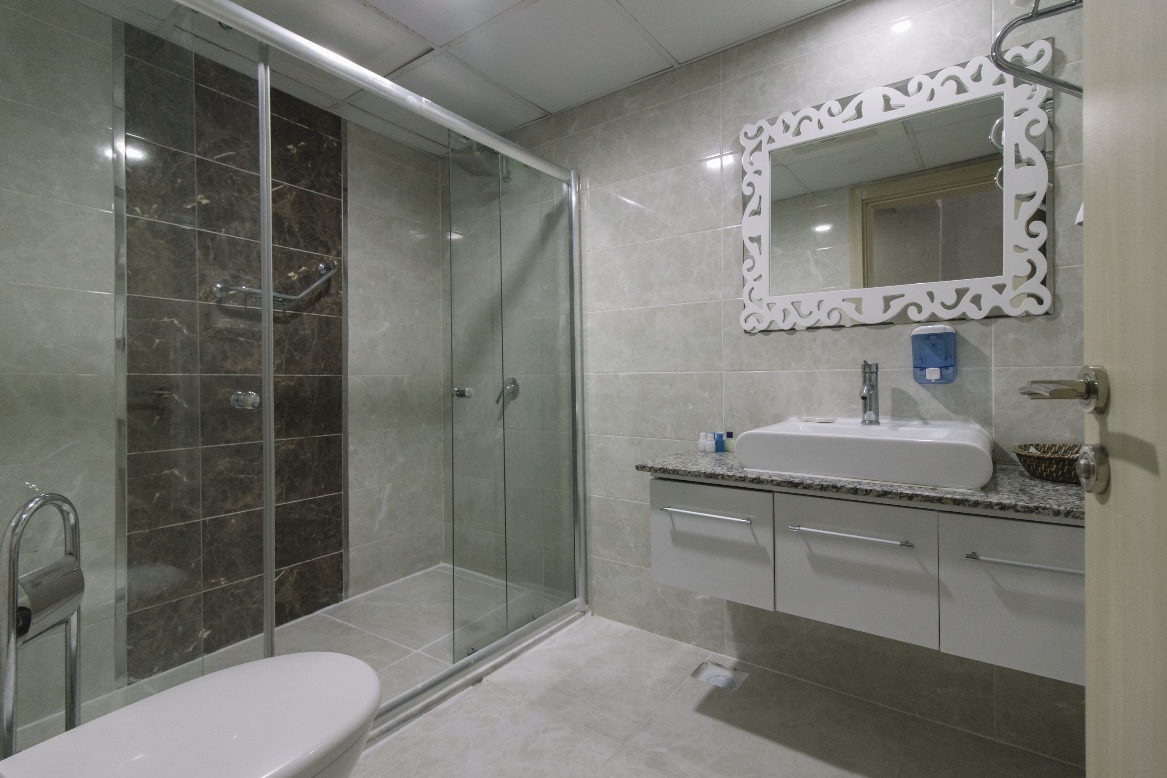 Un baño moderno con ducha envuelta en vidrio, un lavamanos blanco y zona de ducha con azulejos de mármol.
