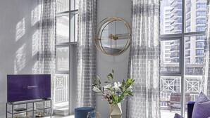 Un salon moderne avec un téléviseur, une horloge ronde dorée et un vase rempli de fleurs.