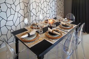 A dining table set with clear glassware, plates, and cutlery, with a geometric patterned wall in the background.