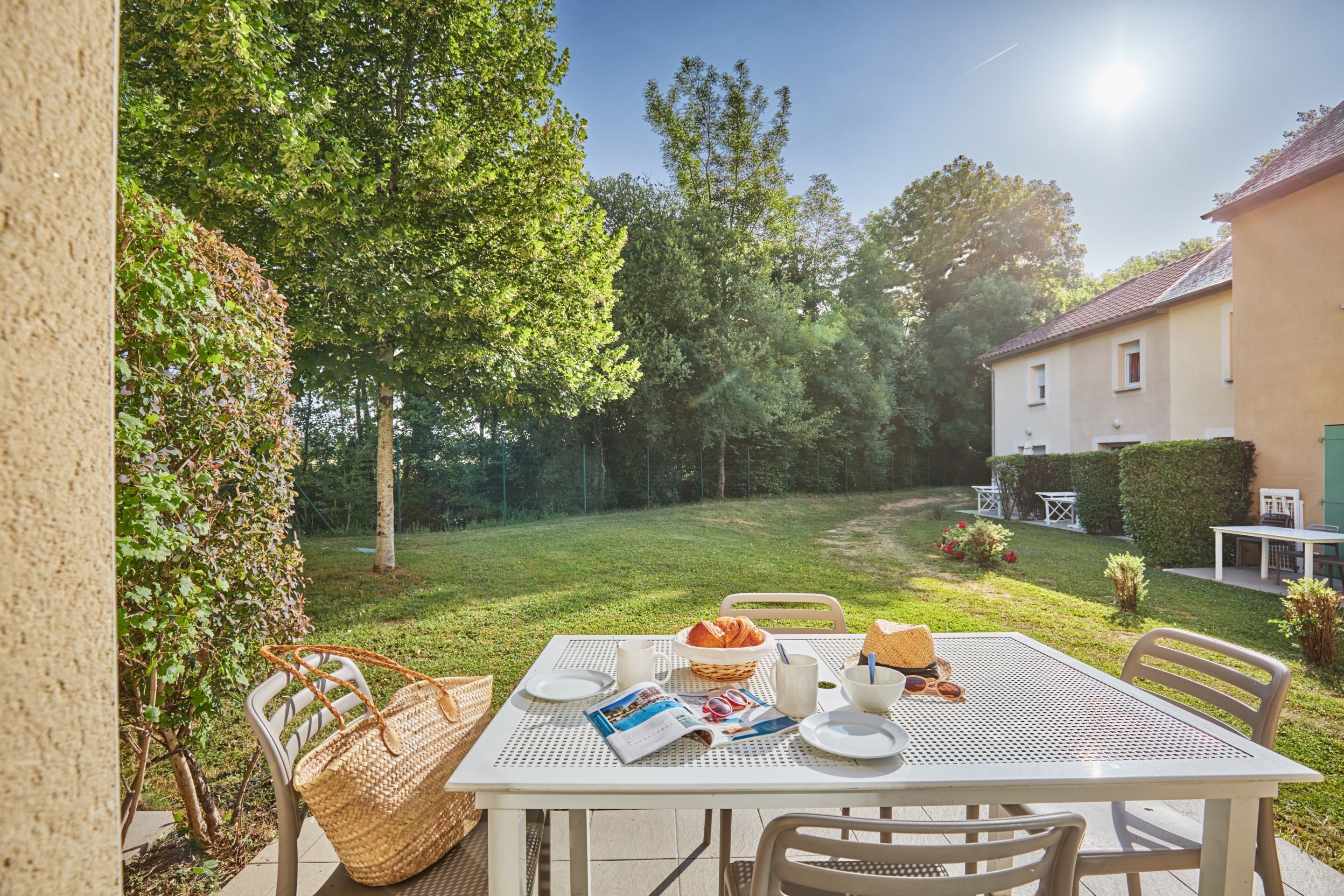 A patio table set with a basket, a magazine, and a croissant.