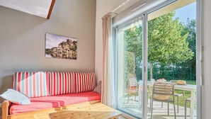 Un salon moderne avec un canapé, une table en bois et une grande porte-fenêtre coulissante donnant sur un espace extérieur aménagé avec une table et des chaises.
