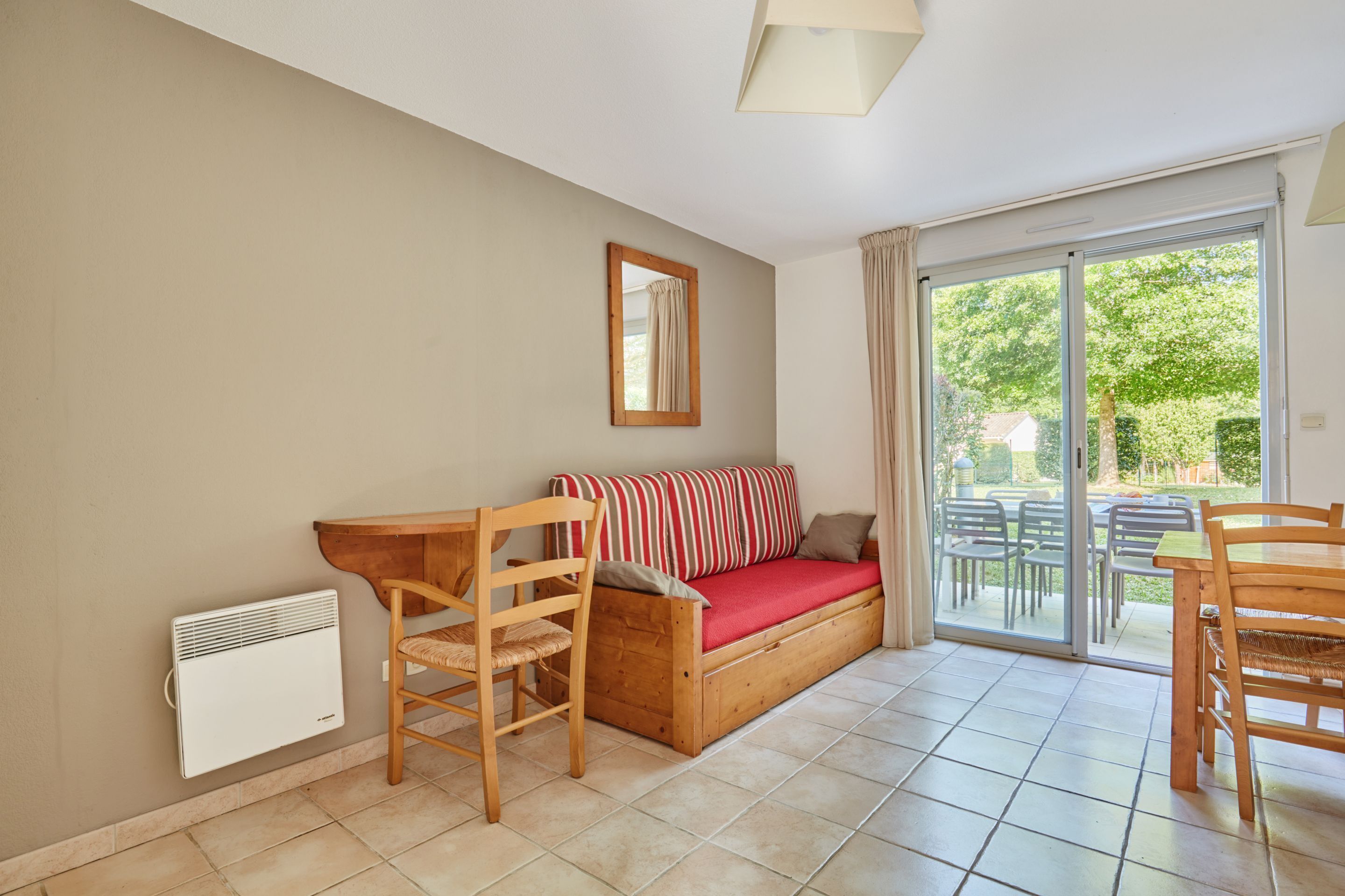 A room with a sofa bed, a wooden chair, a table, and a sliding glass door leading to an outdoor area with chairs.