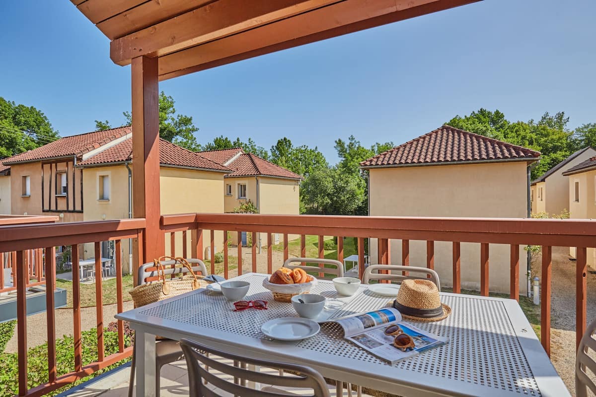 Ein Balkon mit einem Frühstückstisch, komplett mit Croissants, einer Zeitung und einem Strohhut.