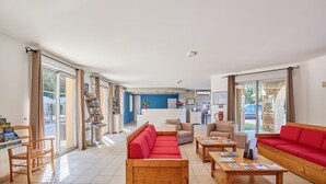 Un vaste espace de vie avec un canapé rouge, une table basse en bois et une cuisine en arrière-plan.
