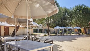 Un espace extérieur aménagé avec des tables et des chaises sous des parasols, entouré d’arbres et d’immeubles.